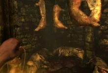First-person view of a dark stone chamber in Amnesia: The Dark Descent, with a hand holding a lantern beneath hanging bodies and a corpse on the floor