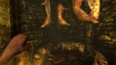 First-person view of a dark stone chamber in Amnesia: The Dark Descent, with a hand holding a lantern beneath hanging bodies and a corpse on the floor