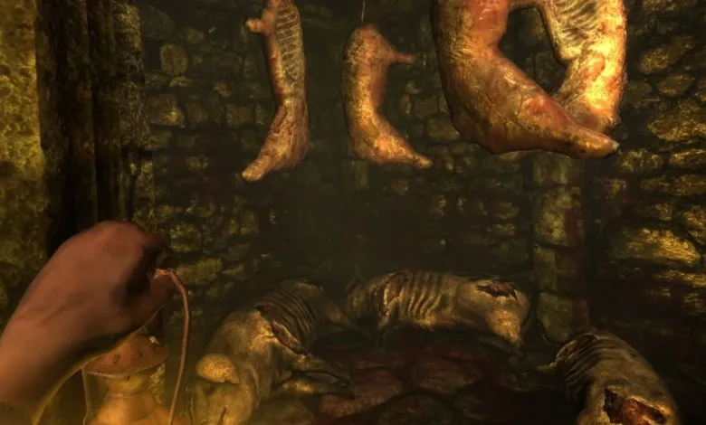 First-person view of a dark stone chamber in Amnesia: The Dark Descent, with a hand holding a lantern beneath hanging bodies and a corpse on the floor