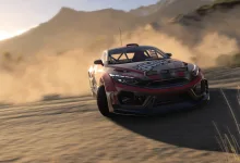 A red-and-black rally car drives across a dusty road with mountains in the background