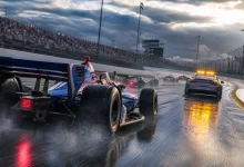 Open-wheel race cars follow a safety car around a wet oval circuit during a caution period.
