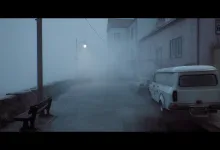 A foggy town street with a parked white van, stone wall, and dim streetlamp in Silent Hill: Townfall