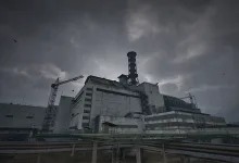 A damaged concrete reactor complex with a tall exhaust stack, construction crane, and industrial pipes beneath dark storm clouds