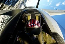 A fighter pilot wearing a Maverick helmet inside a cockpit above Earth
