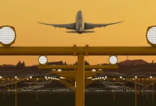 Aircraft taking off above an illuminated airport runway at dusk