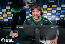 A Counter-Strike 2 esports player wearing a headset competes at a PC station in front of sponsor boards.