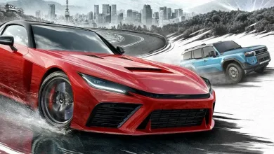 A red sports car drives through water on a mountain road while a blue SUV follows, with a city skyline in the background
