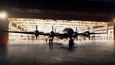 A four-engine bomber sits on a wet hangar floor in front of an illuminated aircraft shelter.