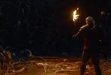 Geralt holds a torch while exploring a dark cavern in The Witcher 3.