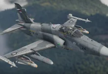 An Indonesian Hawk 209 jet flies over a forested landscape with missiles and other weapons mounted under its wings.