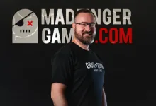A bearded man wearing a Gray Zone Warfare shirt stands before a MADFINGER GAMING.COM graphic.