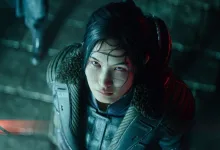 A woman in futuristic armor looks toward the camera in a dark cyberpunk environment.