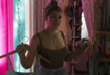 Lucia holds a clothes hanger in a brightly lit room in Grand Theft Auto VI