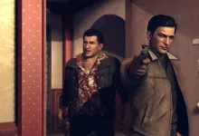 Two men stand in a hallway as one points a pistol toward the viewer in Mafia 2.