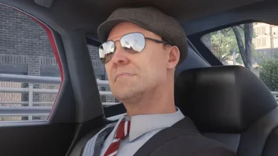A man wearing a flat cap and sunglasses sits inside a car.