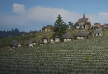 A medieval Manor Lords settlement with a church and houses on a cultivated hillside beneath a blue sky