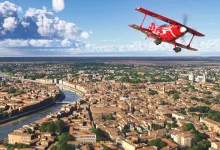 A red biplane flies over an Italian city in Microsoft Flight Simulator 2024.
