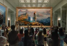 A crowd photographs a large framed game-world scene inside a gallery.