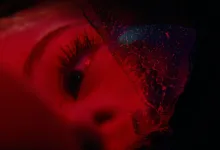 A red-lit close-up of a face partially obscured by a textured material in Precognition.