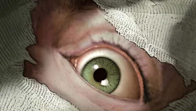 A disturbing green eye peers through strips of gauze in a horror-game scene.