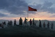A group of wartime figures stands on a ridge beneath a red flag at dusk in The Defiant.