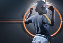 A THE FINALS contestant wearing a gray protective hood, striped shirt, and silver equipment pack in front of a circular orange-lit door.