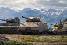 Three armored tanks lined up on a mountain road beside a lake and snow-covered peaks.
