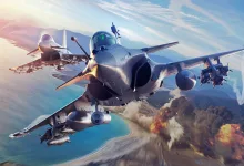 Three fighter jets fly over a coastal landscape with weapons mounted beneath their wings