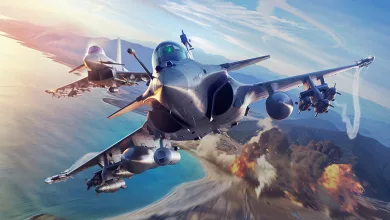Three fighter jets fly over a coastal landscape with weapons mounted beneath their wings