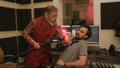 Wes Johnson in a red Sheogorath costume holds a prop beside an audio technician in a recording booth