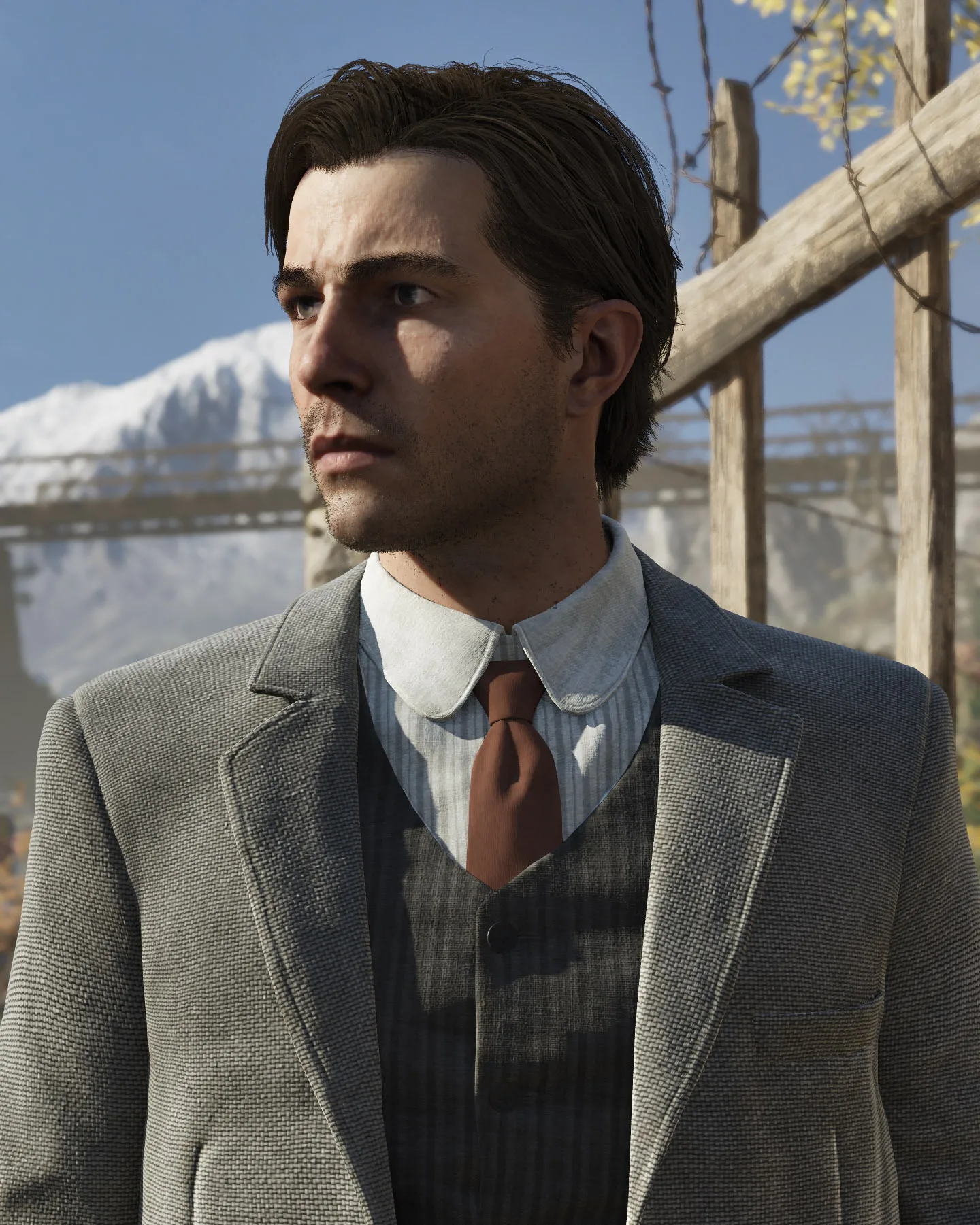 A suited man standing outdoors with snowy mountains behind him