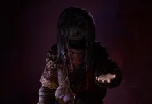 A shadowed character from Daba: Land of Water Scar reaches forward in a dark, purple-lit setting