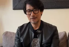 Hideo Kojima wearing glasses and a black jacket while seated indoors