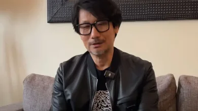 Hideo Kojima wearing glasses and a black jacket while seated indoors