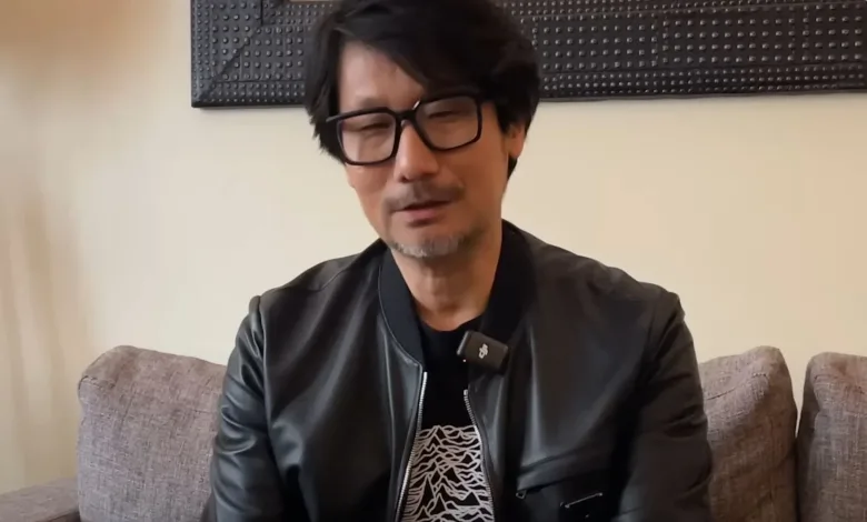 Hideo Kojima wearing glasses and a black jacket while seated indoors