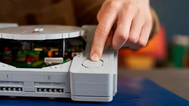 A hand presses a button on a LEGO PlayStation console replica.