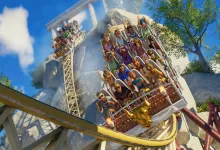 A roller coaster car carries riders around a steep track at a bright outdoor amusement park.