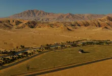 A dry Cities: Skylines II landscape with rocky mountains, scattered cacti, a river, and roads.