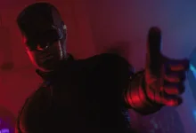Daredevil reaches toward the camera in red and blue lighting.