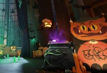 A large black cauldron sits among pumpkins and Halloween decorations in a dimly lit room.