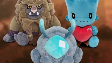 Three Enshrouded plush toys arranged together, including a blue creature holding a red heart