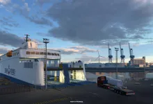 A truck waits beside a large ferry at an Icelandic port in Euro Truck Simulator 2.