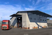 A red truck parked outside a large garage in Euro Truck Simulator 2.