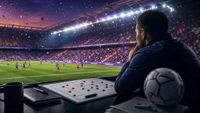 A football manager studies a tactics board while watching a match in a packed stadium.