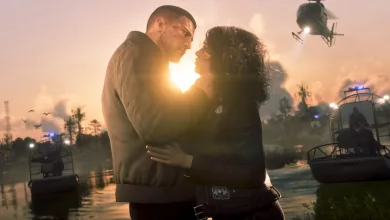 Jason and Lucia embrace by a waterway at sunset, with boats and a helicopter nearby.