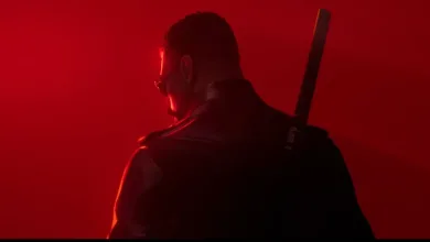 A darkly dressed man with a sword on his back, seen from behind against red light.