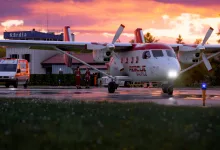 An Antonov An-28 rescue aircraft parked on an airport apron at sunset, with an ambulance nearby.