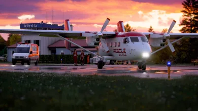 An Antonov An-28 rescue aircraft parked on an airport apron at sunset, with an ambulance nearby.