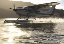 A Carenado CT206 on amphibious floats skims across a lake, throwing up spray.