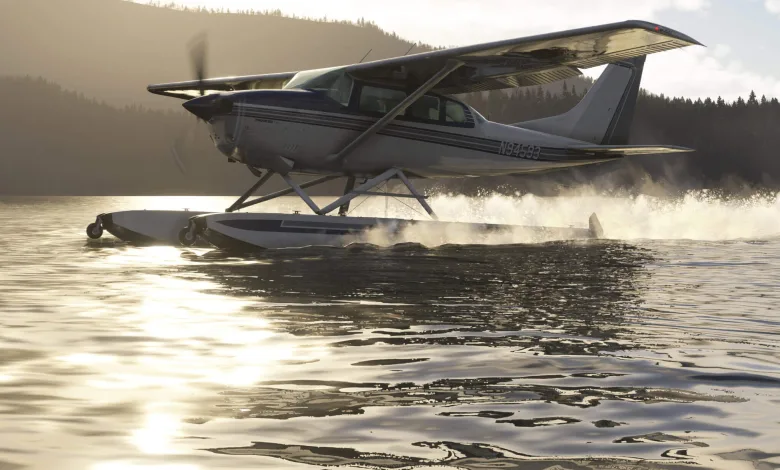 A Carenado CT206 on amphibious floats skims across a lake, throwing up spray.